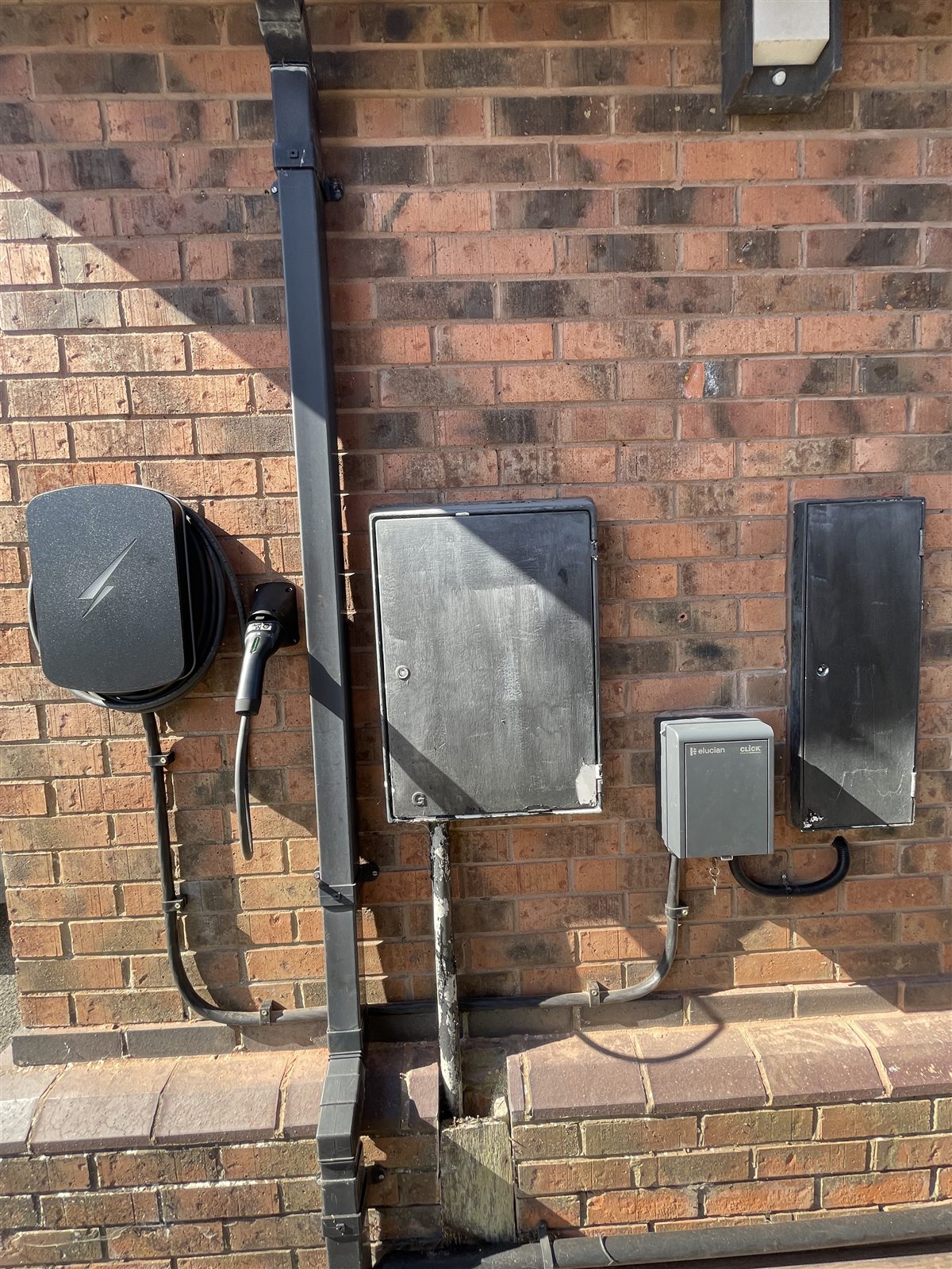 The full wall of a finished install: EV charger, meter cabinets, a wall-mounted isolator unit and the conduit run between them.